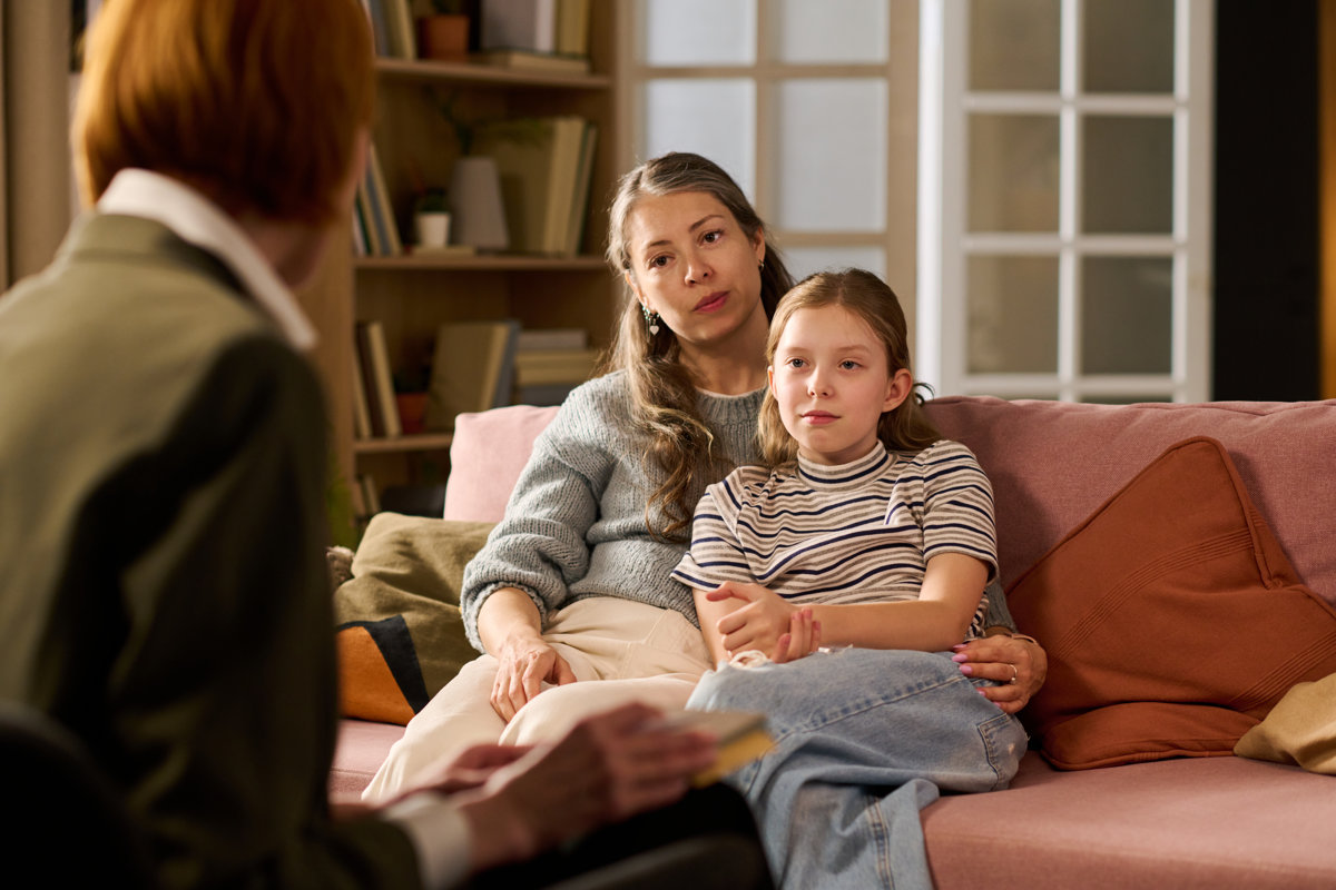Caucasian mother and daughter sitting together, listening during counseling session with female therapist, showing family support and child mental health care. Useful for therapy services promotion