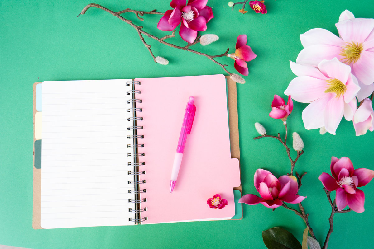 Blooming pink magnolia tree branch with flowers against green background, open notebook page for copy space